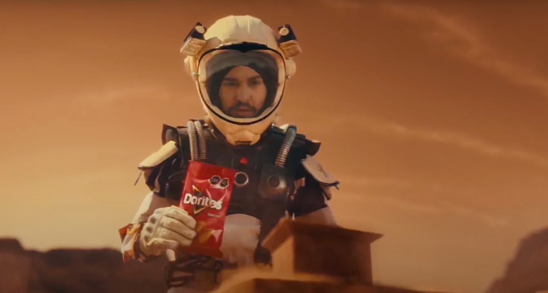 Doritos México imagina en Marte un lugar para celebrar a quienes desafían lo establecido Persona disfrazada de astronauta con una bolsa de Doritos en la mano