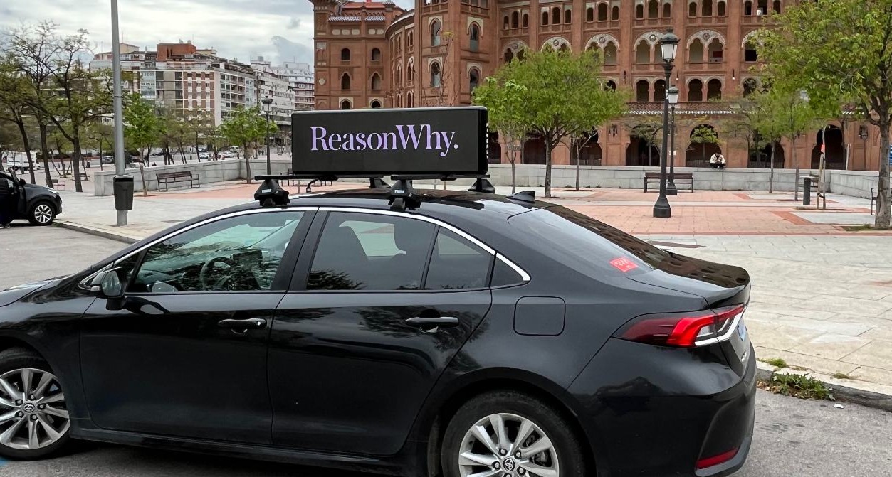 coche negro con una pantalla sobre el techo que incluye el logotipo de Reason Why
