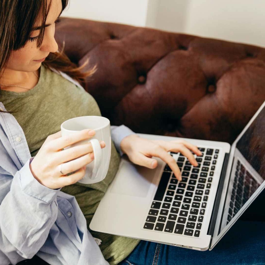 Chica consulta ordenador mientras sujeta una taza en la mano