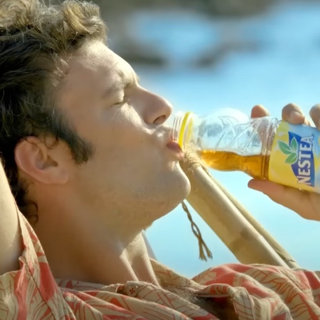 un chico bebiendo nestea en la hamaca de la playa