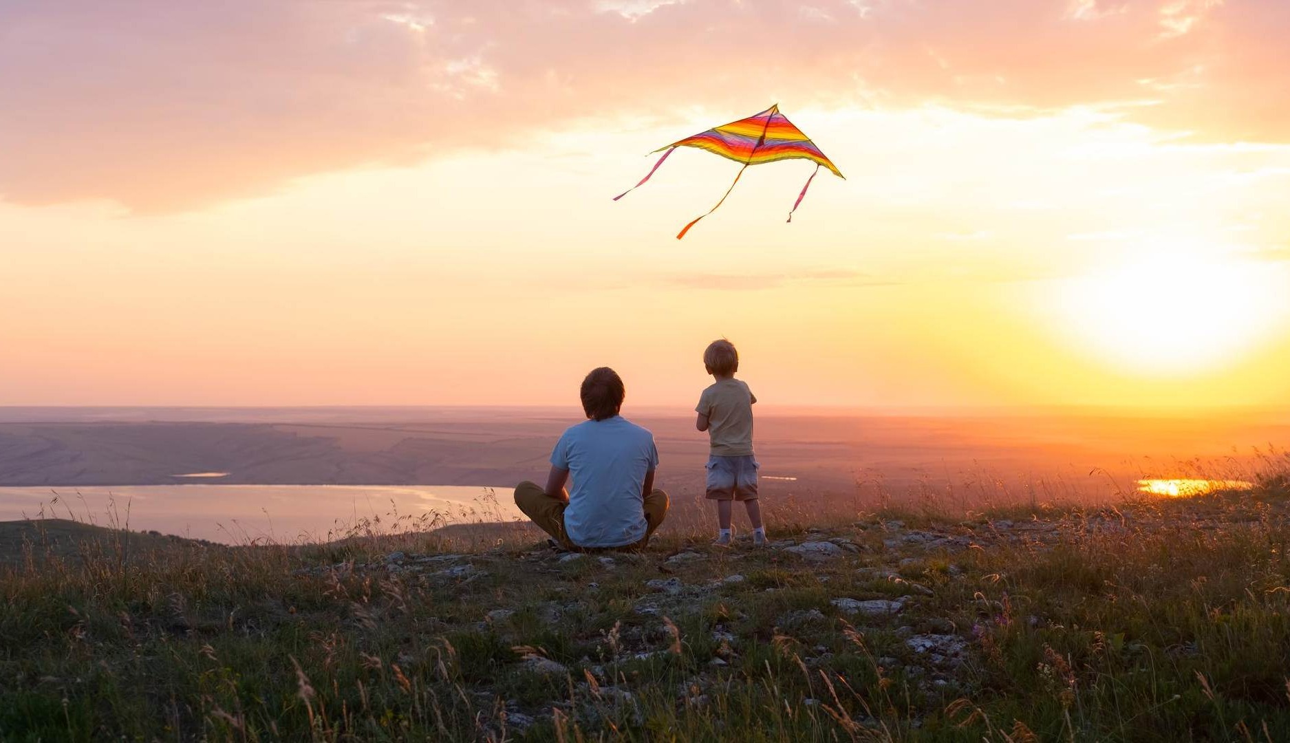 Hombre y niño vuelan una cometa al atardecer