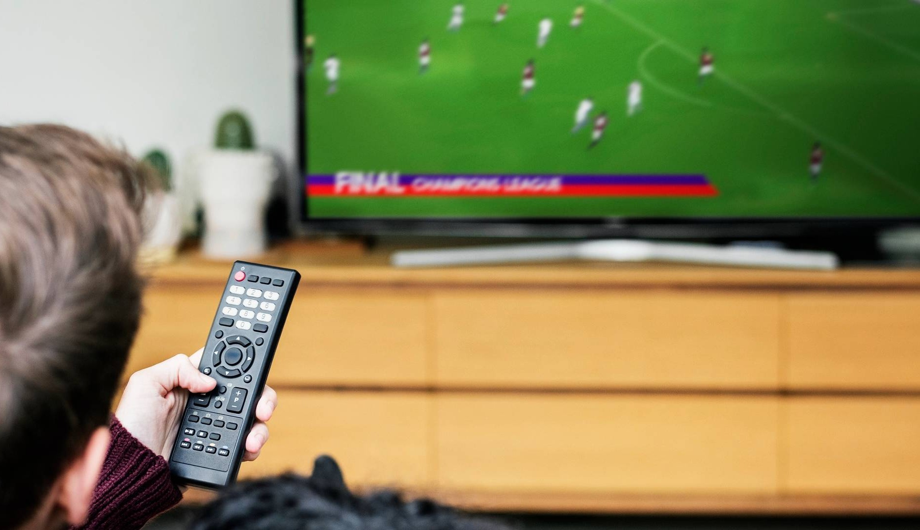 Hombre con mando a distancia en la mano viendo fútbol en televisión