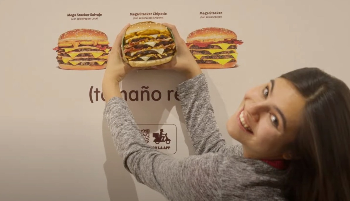 Una chica cogiendo la hamburguesa en la valla de Burger King