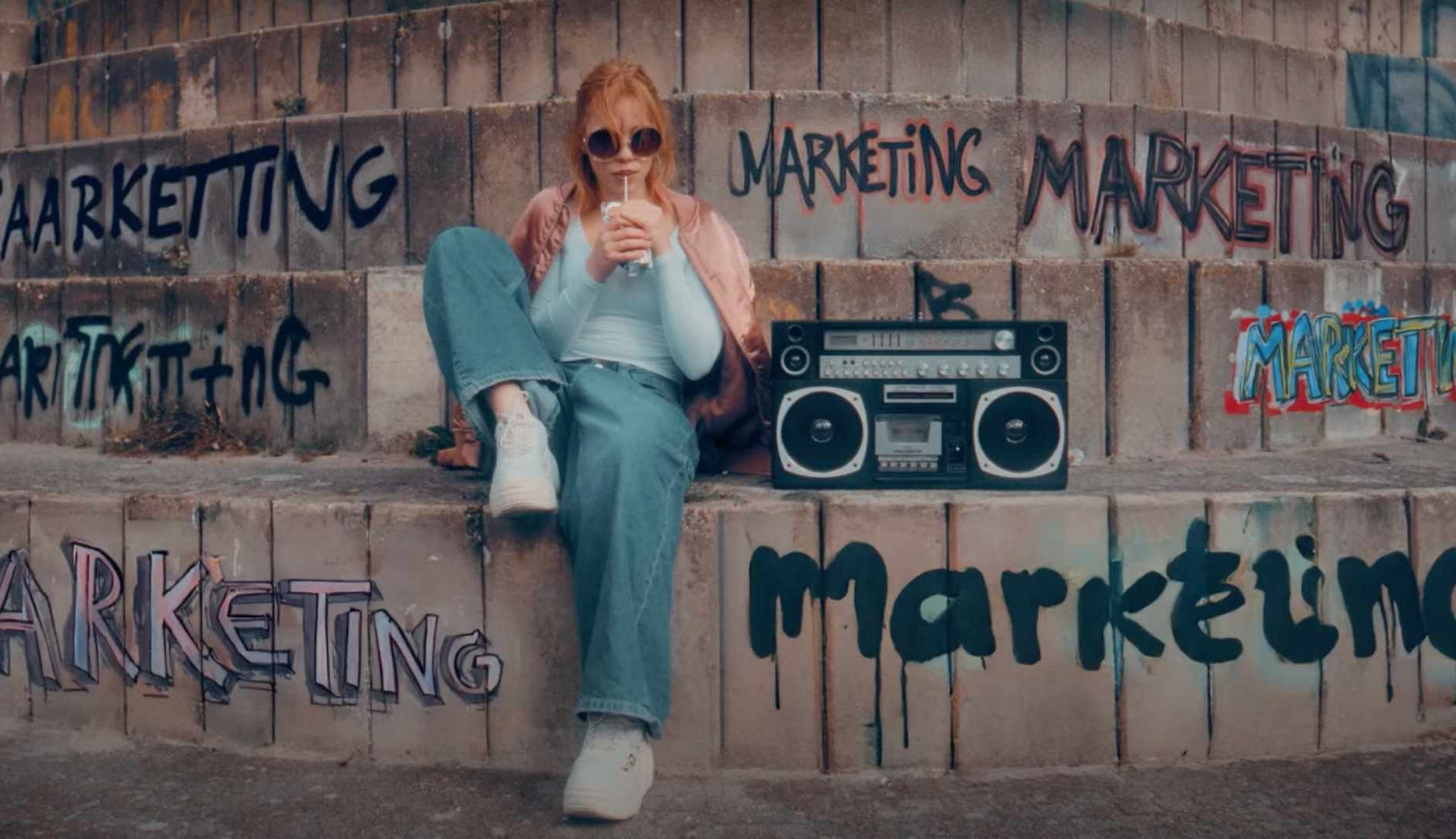 Una chica sentada junto a una radio y rodeada de grafitis con la palabra marketing