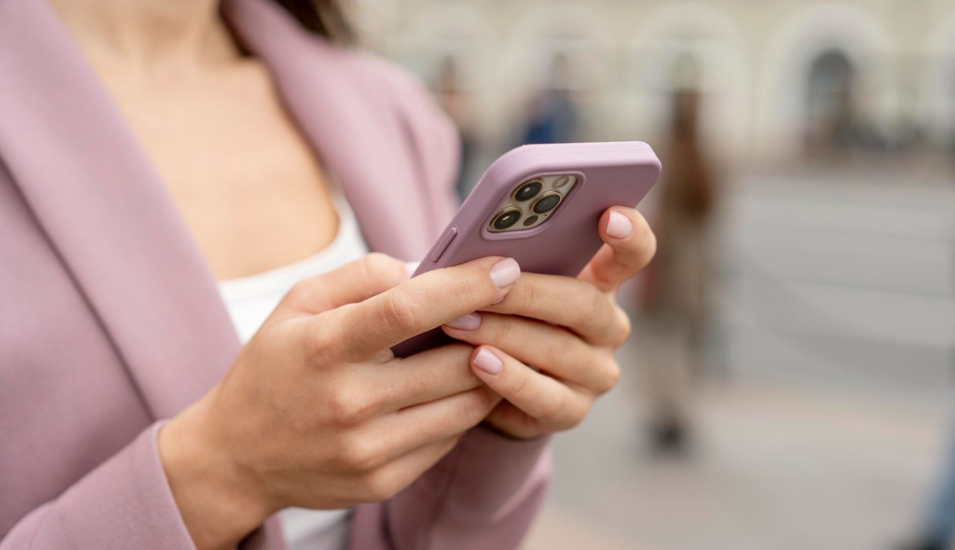 Mujer con chaqueta rosa sujeta un teléfono móvil del mismo color