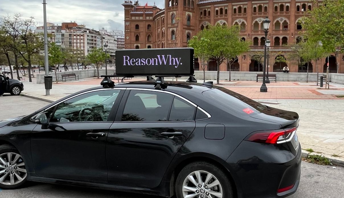 coche negro con una pantalla sobre el techo que incluye el logotipo de Reason Why
