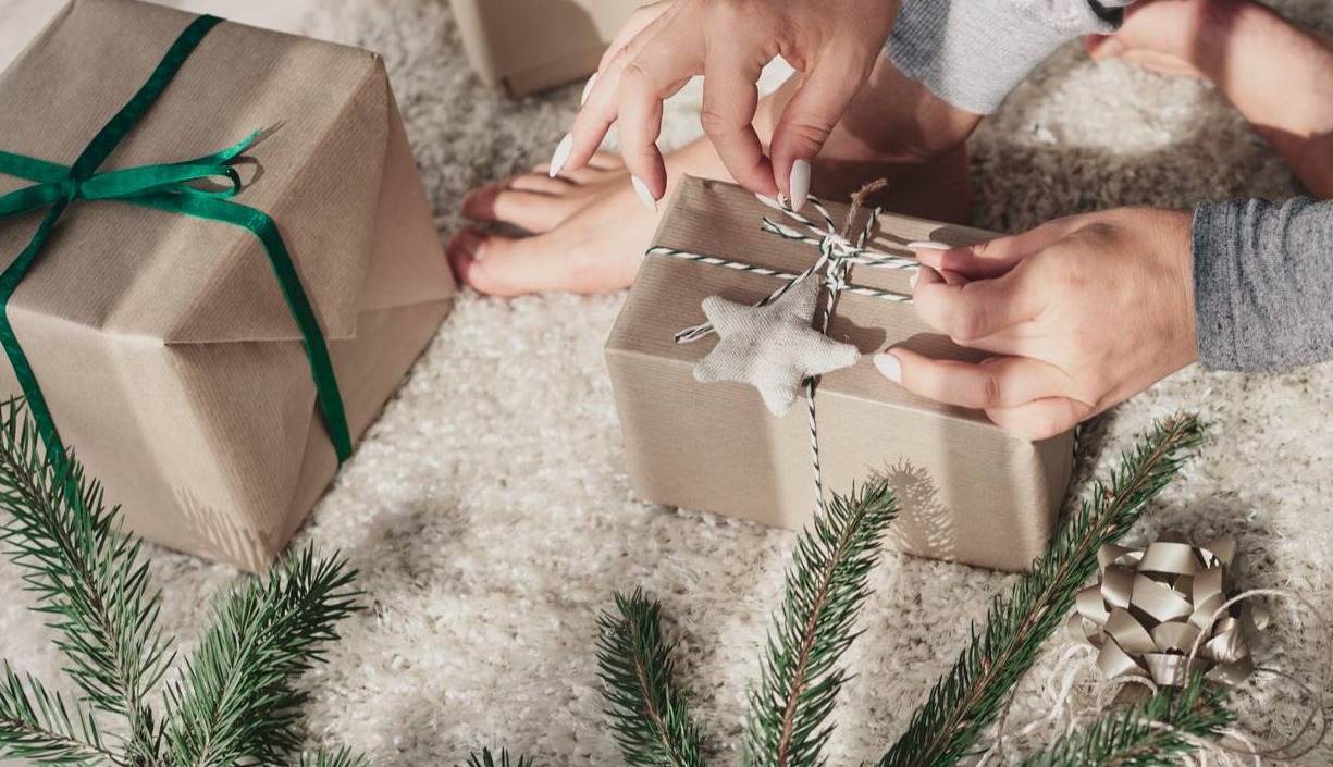 unas manos envolviendo un regalo de Navidad junto al árbol