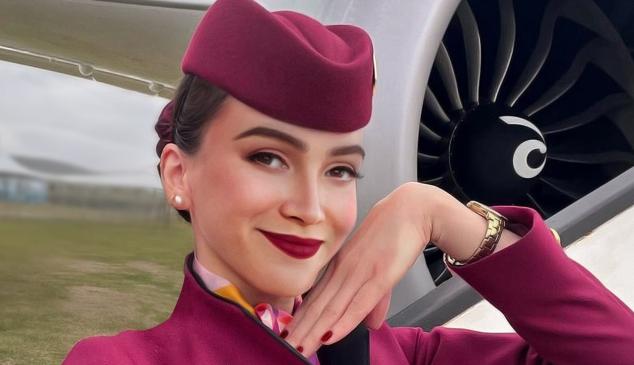 Una azafata vestida con el uniforme de Qatar Airways posando con la mano junto a la mejilla