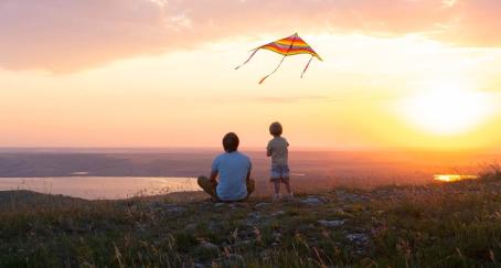 Hombre y niño vuelan una cometa al atardecer