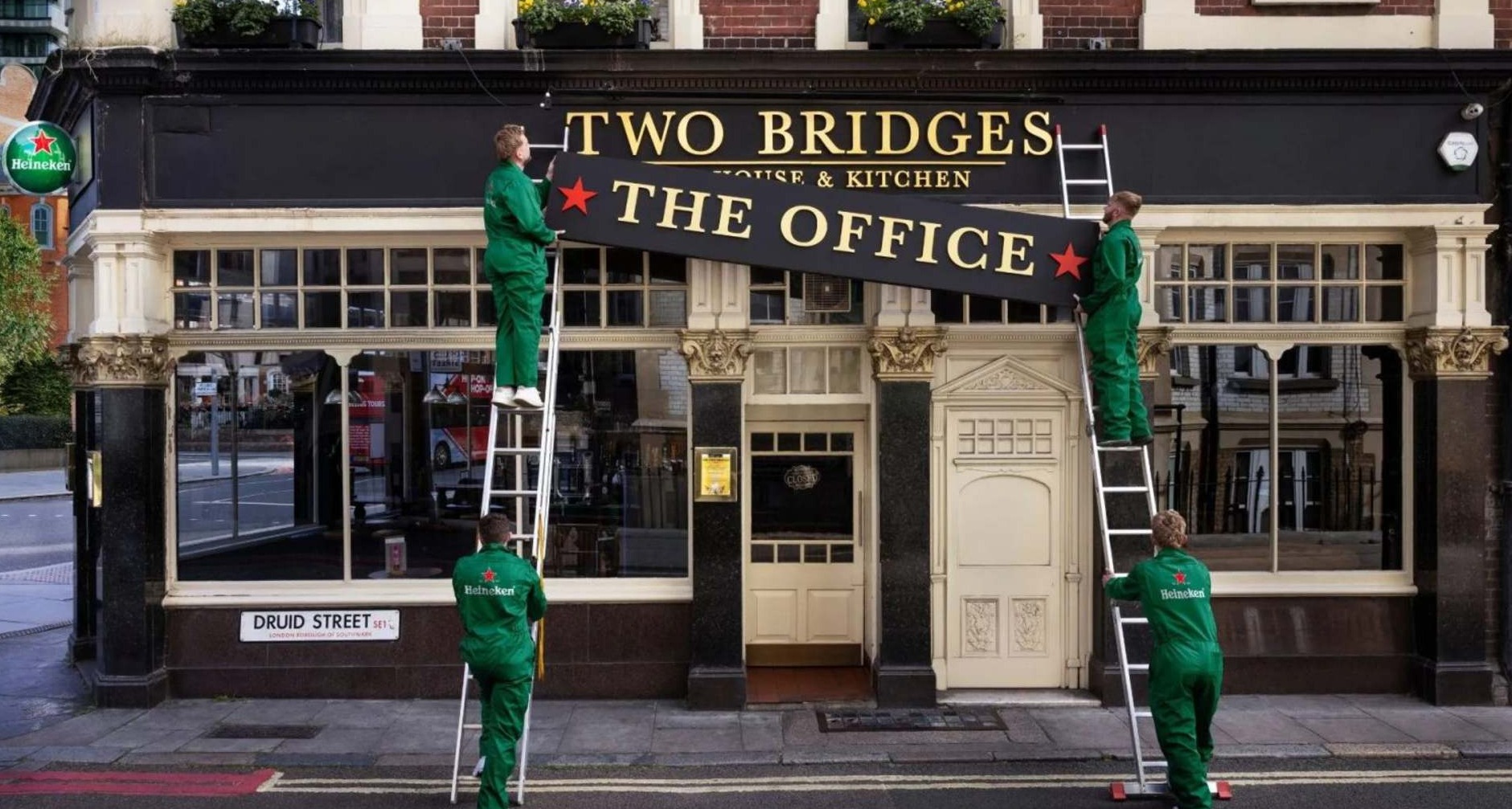 Heineken celebra el trabajo presencial convirtiendo los pubs en extensiones de la oficina Trabajadores con monos de Heineken colocan un cartel en la fachada de un pub