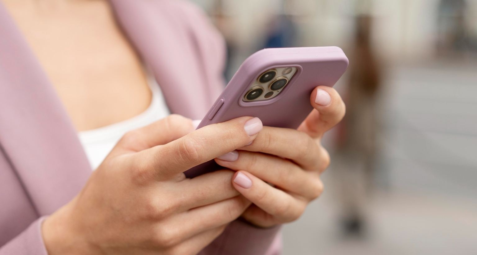 Mujer con chaqueta rosa sujeta un teléfono móvil del mismo color