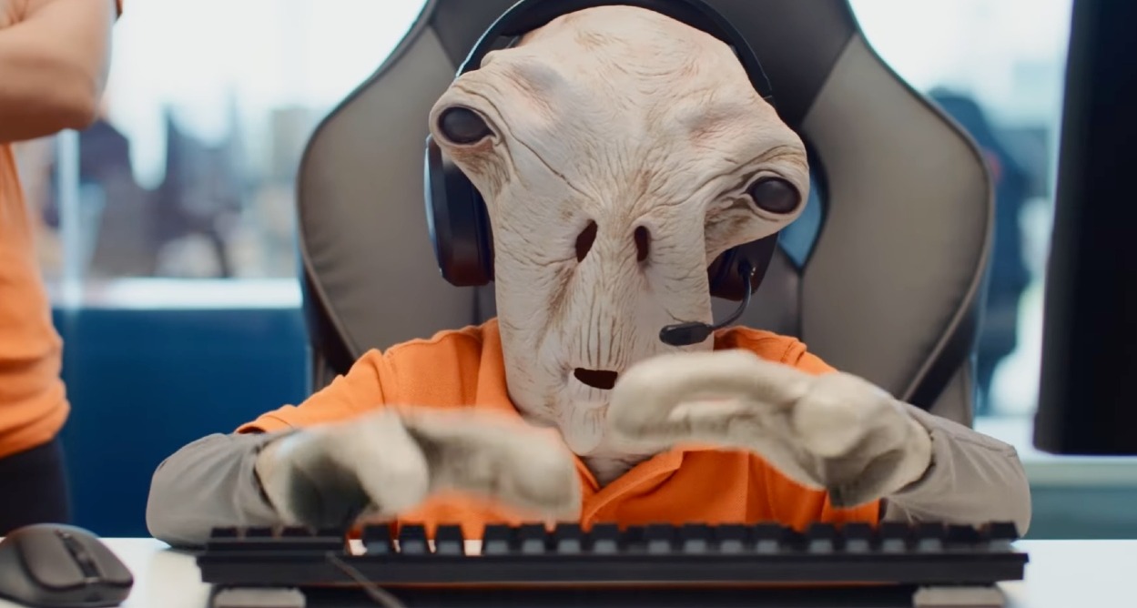PcComponentes lanza “Marcianos vs Murcianos”, una campaña que refuerza su trato humano un marciano vestido con el uniforme de pccomponentes sentado delante del ordenador con unos auriculares de centralita