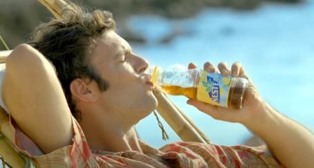 un chico bebiendo nestea en la hamaca de la playa