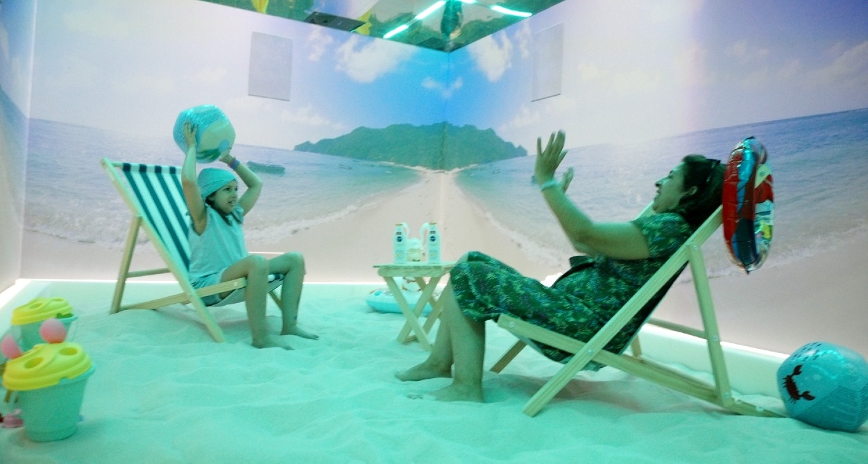 La Fundación Juegaterapia instala una playa en su sala inmersiva para acercar el verano a niños con cáncer una madre y su hija juegan a la pelota en la sala inmersiva con arena y tumbonas