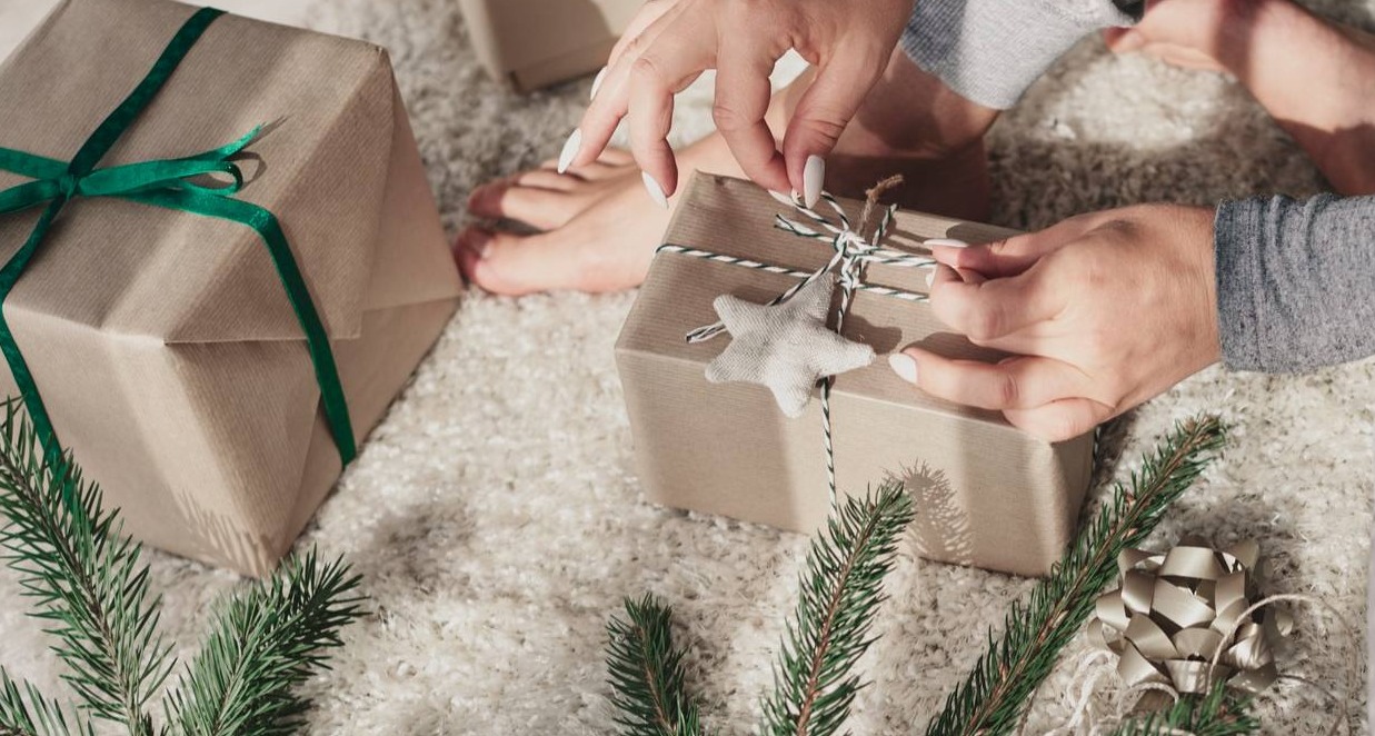 unas manos envolviendo un regalo de Navidad junto al árbol