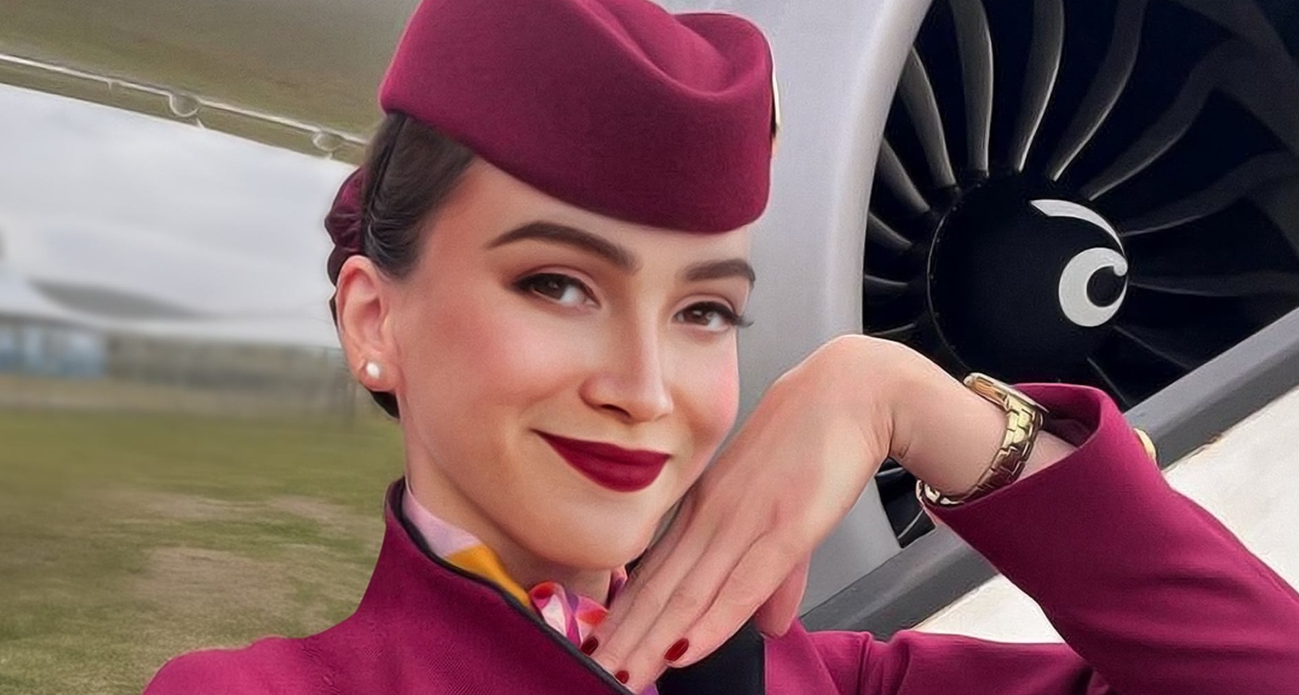 Una azafata vestida con el uniforme de Qatar Airways posando con la mano junto a la mejilla